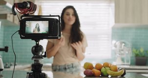 Woman, camera and live streaming in kitchen, broadcast and tutorial or teaching at home. Female influencer, webinar and vlogger or technology for video recording, jar and fruit for nutritional diet