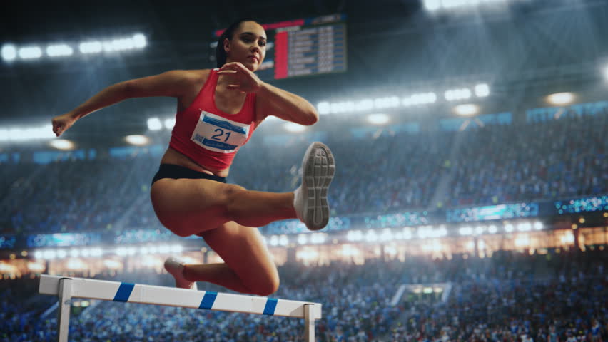 Cinematic Slow Motion Footage of Hurdling with Speed Ramp Effect. Strong Female Athlete is Running Towards an Obstacle, Jumping Over the Barrier while Sprinting in a Race at a Crowded Stadium