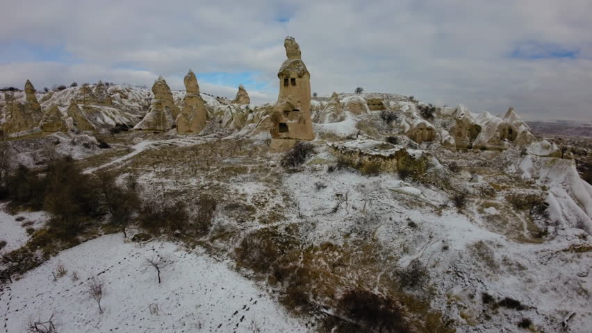 Aerial Shot Of Flock Of Birds On Top Of Ancient Rock Hoodoo On Snowy Volcanic Landscape Under Clouds During Winter - Cappadocia, Turkey