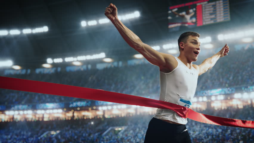Cinematic Slow Motion Footage of a Runner with Speed Ramp Effect. Strong Male Athlete is Sprinting Towards the Line in a Crowded Stadium, Crossing the Race Finish with His Hands in the Air