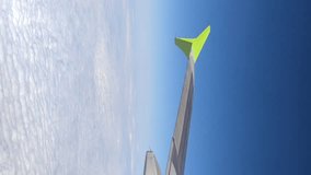 View through passenger airplane window of flying in the sky aircraft's wing in a sunny day. Clear blue sky with white clouds. Real time vertical video. Air travel and transportation theme.