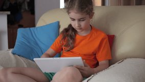 Portrait of Cute Girl Playing Game on Tablet PC Relaxing in Living Room. Child Browsing Social Media. Child Using Tablet PC Sitting on Sofa at Home, Homeschooling, Distant Remote Education.