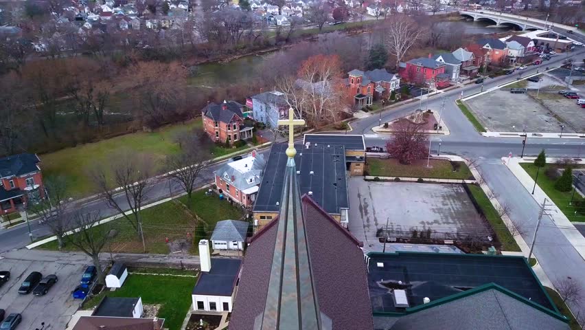 Aerial view circling Logansport church steeple cross overlooking Indiana small town community