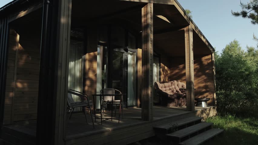 Cozy terrace in the wooden tiny house. Terrace in a small country house in the forest at summer. Table and brown sofa, shadows from trees on the wooden wall, slow motion.