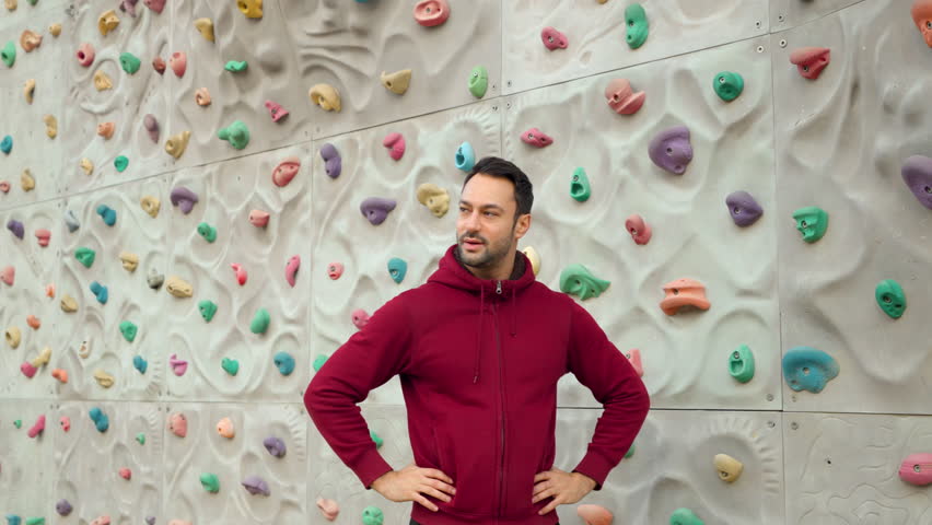 Man Climber Heavily Breathing After Exercising on Climbing Wall at Outdoor Sport Ground, Hands on Waist Pose