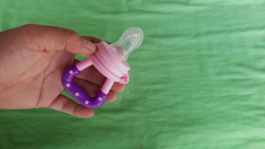 Pink silicone baby pacifier held by a person on a green background Royalty-Free Stock Footage #3401869149