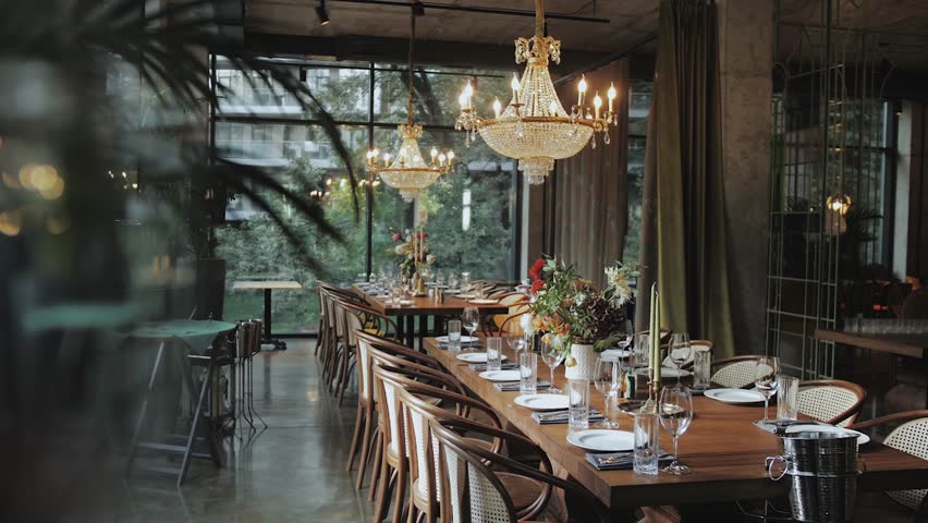Beautiful wedding decor floral composition on the table, switched on chandeliers hang over the table. White plates, candles, wine glasses on the table, slow motion.