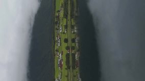 Small Town and Reflection in Lake. Green Landscape of Norway in Cloudy Summer Day. Aerial View. Drone is Flying Sideways and Ascending. Vertical Video