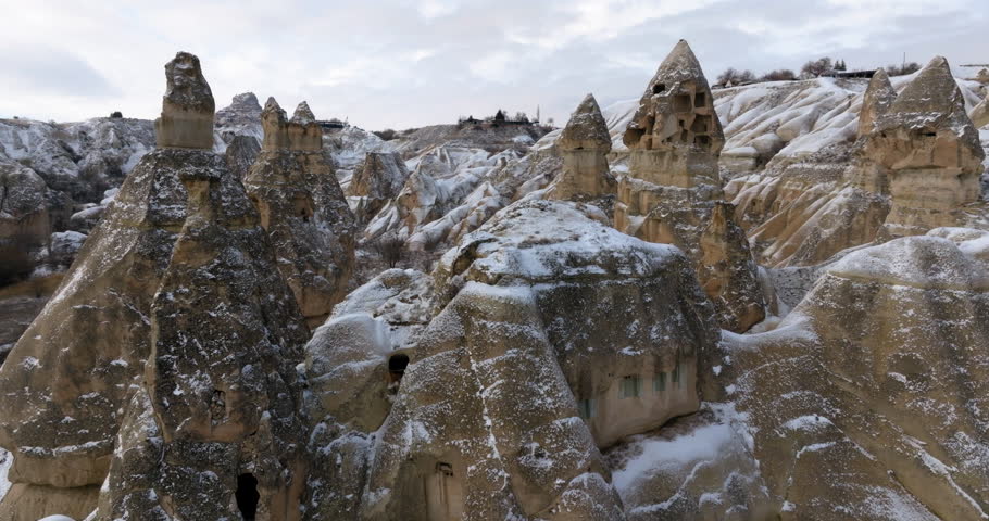 Aerial Forward Shot Of Historic Cave Houses On Rock Hoodoos In Snowy Weather Under Cloudy Sky - Cappadocia, Turkey