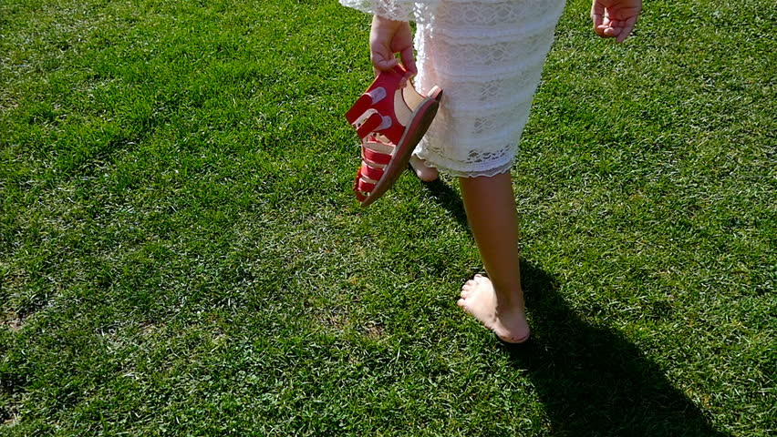 Girl in white dress bare feet walking over green grass, freedom concept, slow motion