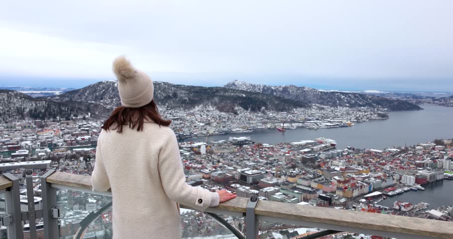 A tourist woman enjoys the panoramic winter view of the snow covered cityscape of Bergen