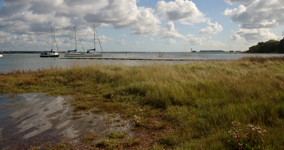 Wide shot of low lying grass flooded at high tide taken at Ashlett creek sailing club in the Solent, Southampton. Calshot in background. Royalty-Free Stock Footage #3402118173