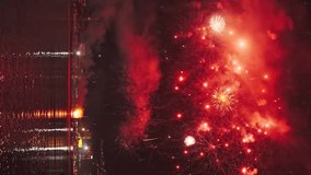 Bright fireworks exploding with colorful lights over sea shore and small mediterranean town. Vertical video