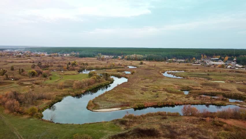 Aerial tilt down view on river curve in autumn valley with reeds, trees, dirt road. Siverskyi Donets River in Ukraine