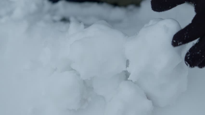 Slowmotion closeup of grabing and removing pile of snowballs with black gloves