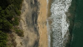 Vertical video of Birdeye aerial view of black and white beach with waves, going along coast
