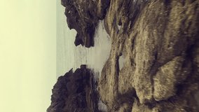 Low angle extremely fast flying over the rocks to the sea. Vertical Video