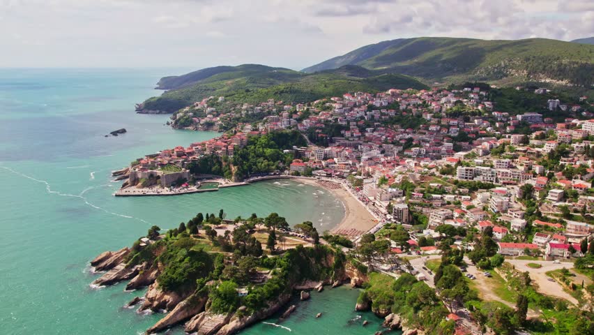 Drone flying above the beautiful city of Ulcinj in Montenegro during the summer season. Old city stone houses and people swimming at the beach of the Adriatic Sea.  Royalty-Free Stock Footage #3402491501