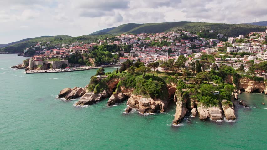 Drone flying above the beautiful city of Ulcinj in Montenegro during the summer season. Old city stone houses and people swimming at the beach of the Adriatic Sea.  Royalty-Free Stock Footage #3402494733