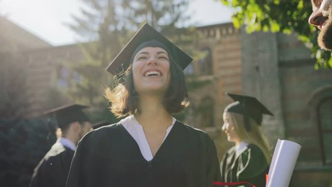 Young multi ethnical graduates in caps laughing out loud and having fun on their graduation day. Outdoors. Close up