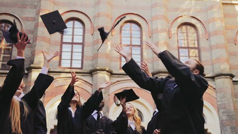 Group of multi ethnical graduates in traditional clothes tossing their caps up in the air happily in front of the University. Outdoors