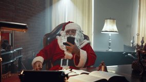 Santa sits on a chair and puts his legs up on the desk, relaxes while using a mobile phone - Powered by Shutterstock - Get 15% off with code: PIKWIZARD15