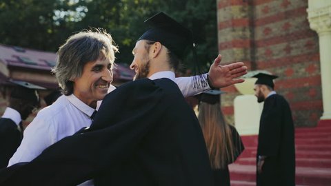 Handsome male graduate hugging with his father, dad congratulating his son with a graduation from University. Outdoor