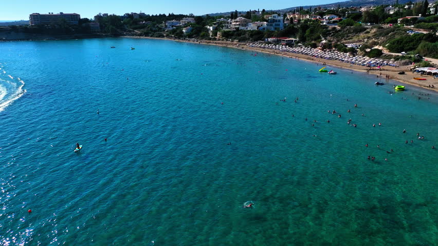 Aerial Panning Scenic Shot Of Tourists In Wavy Ocean At Beach On Sunny Day - Paphos, Cyprus