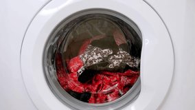 Closeup footage of washing machine door with spinning laundry