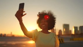 Video of a happy african woman waving at the camera during a video call standing in the city during sunset
