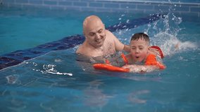 family in the pool. dad and son. slow-motion video. dad in the pool teaches the child to swim. High-quality shooting in 4K format