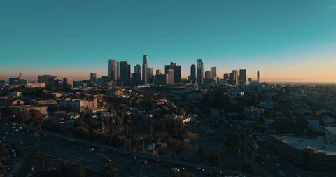 Cinematic aerial drone footage of downtown urban Los Angeles with city skyline, freeway and traffic below.