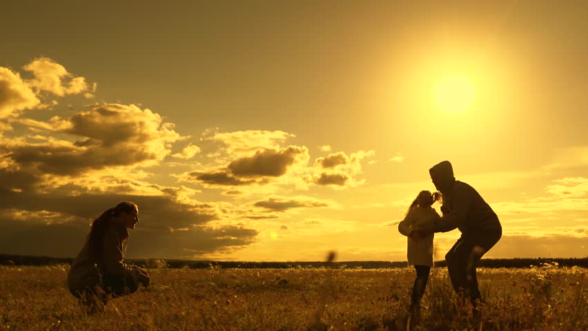 Child runs from father to mother, hugs parents, family game. Happy family Weekend, dad spins his daughter in his arms in park under sun. Family walks in park. Parents, kid in nature. People outdoors