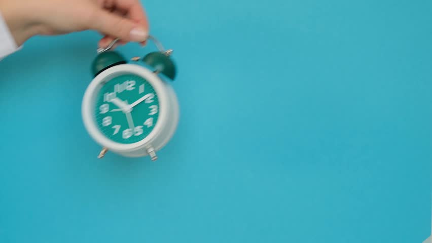 Hand holding a classic alarm clock on a blue background. 4k footage
