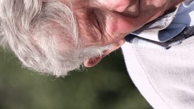 Portrait of an old gray-haired grandfather fixing his hair with his hand and looking at the camera. Vertical video