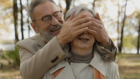 Elderly man surprising woman in autumn park mature husband closing wife eyes with arms senior Caucasian couple laughing enjoy meeting outdoors retired family love romantic moments happiness in old age - Powered by Shutterstock - Get 15% off with code: PIKWIZARD15