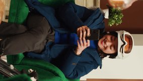 Vertical Video Asian woman laughing at smartphone and talking to friends about extreme winter sport with skis, preparing to go sliding on mountain alpine slopes. Young adult checking online websites - Powered by Shutterstock - Get 15% off with code: PIKWIZARD15