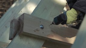 Close-up of builder drilling wooden structure. Clip. Man drills wooden beams of house under construction. Construction of wooden country house