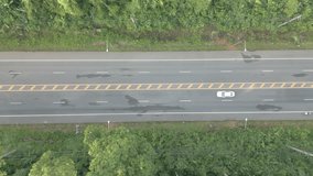 The video shows a drone slowly flying from right to left, capturing a wide road with cars driving smoothly while surrounded by lush forests.4k