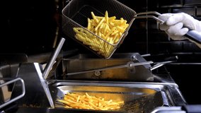 Close up of french fries is cooking into deep fryer. Crunchy potatoes is frying in hot boiling oil at cuisine. Process of making fast food at kitchen. Food preparing concept.  Slow motion
