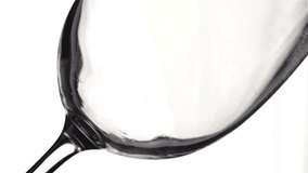 Close-up of filling wine glass with red wine in super slow motion. Pouring red wine into goblet. Red wine forms beautiful wave in glass on white background

