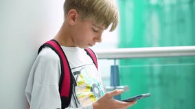 Calm teenage boy with a backpack uses the phone, leaning against a column, waiting for friends to party at the mall - Powered by Shutterstock - Get 15% off with code: PIKWIZARD15
