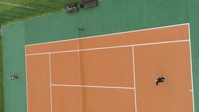 Elderly people are playing tennis on court in green park. Aerial view. Vertical Video