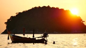 Travel Video silhouette long tail boat converted to boat excursions floating in the andaman sea with golden light of the Sun before sunset in travel or transportation concept