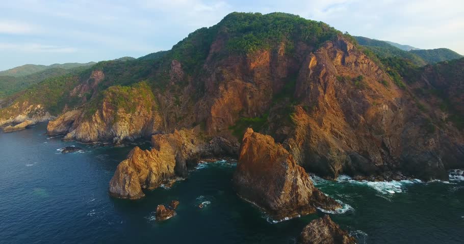 Mountainous cliff face along the coast of Mexico straight down into the dark blue ocean water of Carrizal anchorage during golden hour