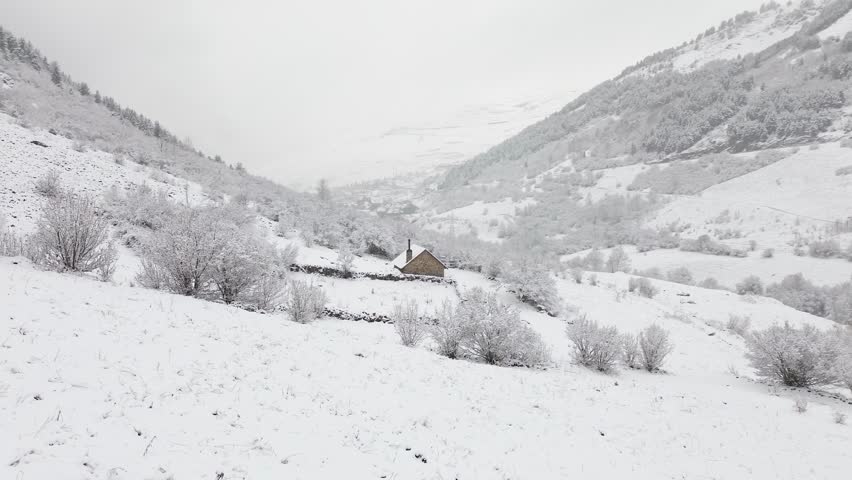Aerial shot of a lonely snowy rustic house in the middle of the mountains of a valley in the Spanish Pyrenees on a cloudy day