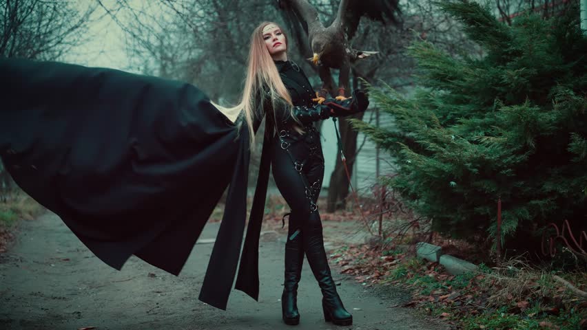 art portrait fantasy woman warrior holding fly white-tailed eagle wild bird on hand. Princess girl long blond hair. Lady queen assassin hunter black dress armor walking along street dark trees fog. 4k