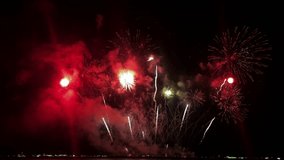 Multi-colored pyrotechnics bursting in a rhythmic fashion and filling the night sky with bright lights, at an international fireworks festival in a tourist destination in Southeast Asia.