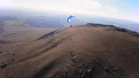 Aerial view from a sports FPV drone. A paraglider athlete flies near the slopes of a small mountain. Free paragliding flight over rural fields in autumn Video from FPV drone