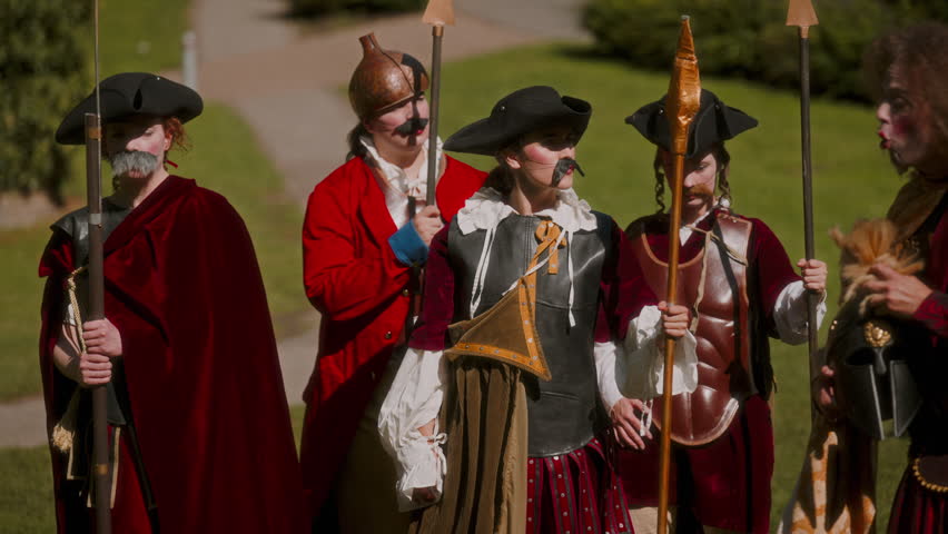 An authoritative general leads a group of footmen wielding spears in a theatrical performance outdoors
